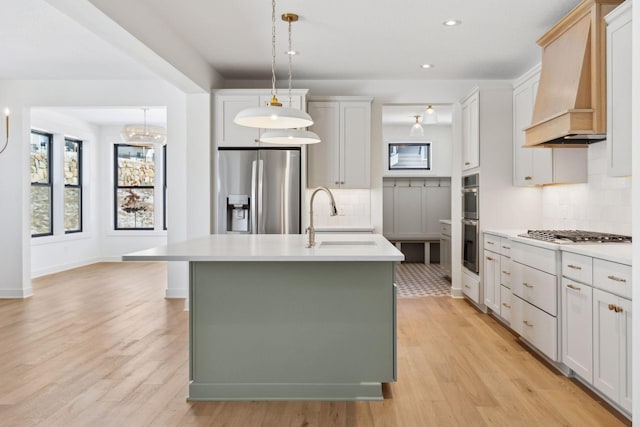 kitchen with a center island with sink, custom exhaust hood, light countertops, appliances with stainless steel finishes, and white cabinetry