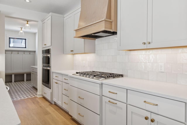 kitchen featuring decorative backsplash, custom exhaust hood, light countertops, stainless steel appliances, and white cabinetry