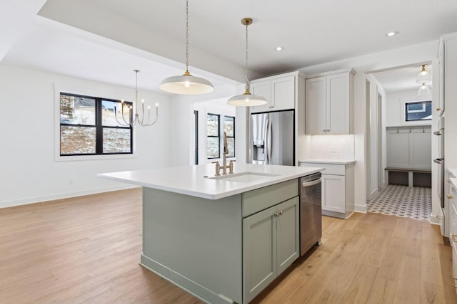 kitchen with decorative backsplash, an island with sink, appliances with stainless steel finishes, light countertops, and a sink