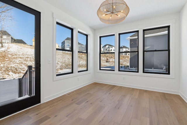 unfurnished room featuring a healthy amount of sunlight, light wood-style flooring, visible vents, and a chandelier