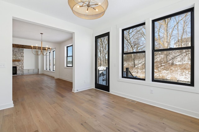 entrance foyer featuring light wood-style flooring, a notable chandelier, a fireplace, visible vents, and baseboards