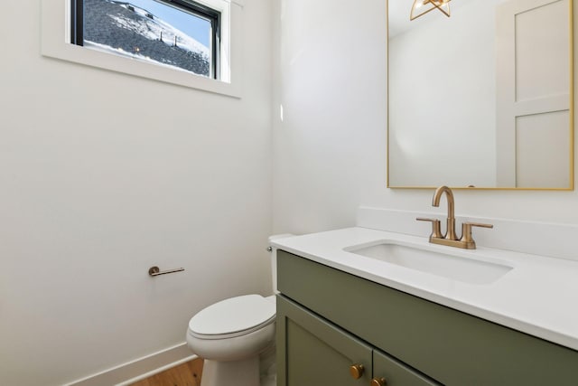 half bath with wood finished floors, vanity, toilet, and baseboards