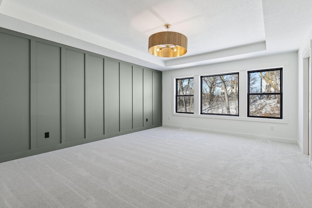 unfurnished room featuring baseboards, a tray ceiling, a textured ceiling, and light colored carpet