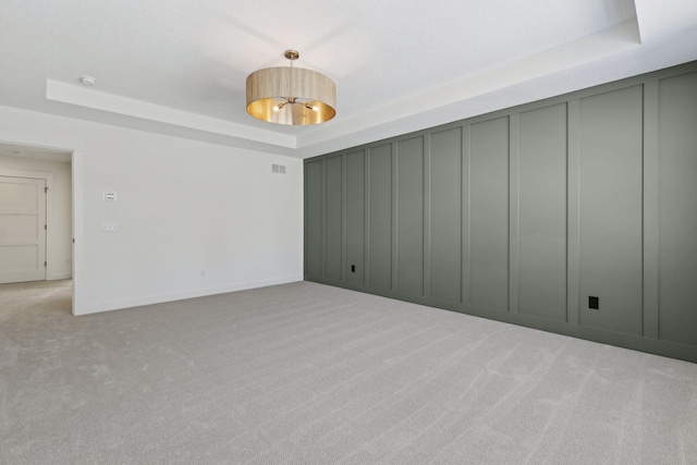 empty room featuring a tray ceiling, light colored carpet, a decorative wall, and visible vents