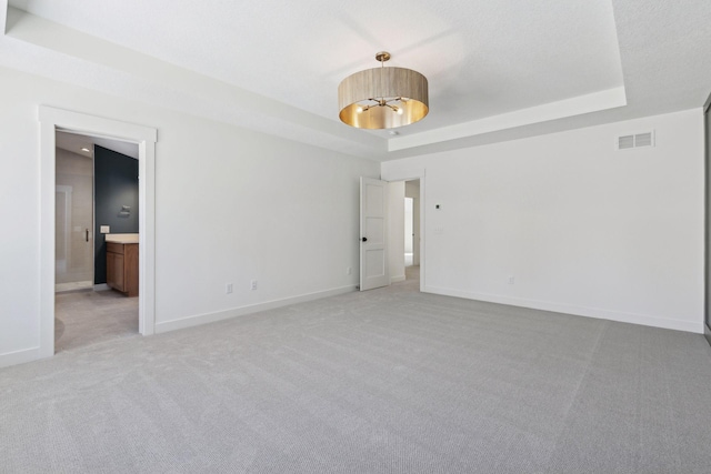 spare room featuring light carpet, a tray ceiling, visible vents, and baseboards