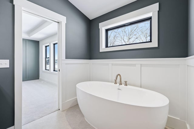 bathroom with a freestanding tub, a decorative wall, and a wainscoted wall