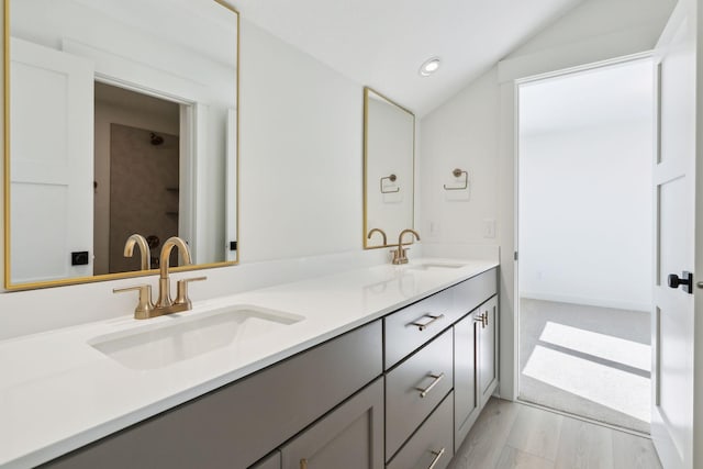 bathroom featuring double vanity, vaulted ceiling, a sink, and wood finished floors