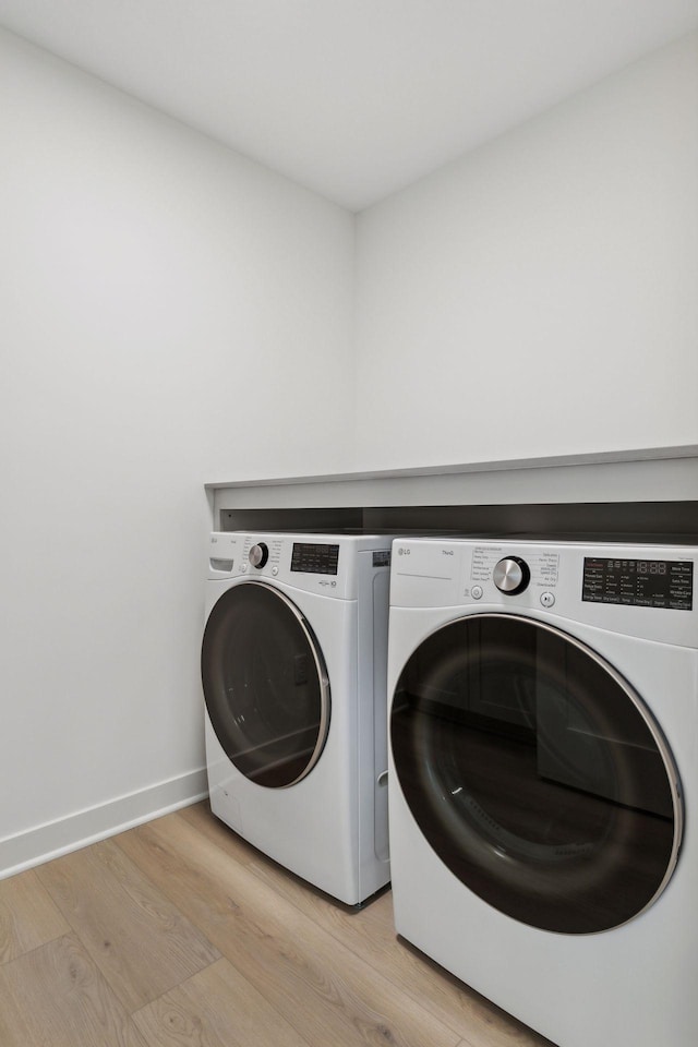 laundry area featuring light wood finished floors, laundry area, separate washer and dryer, and baseboards