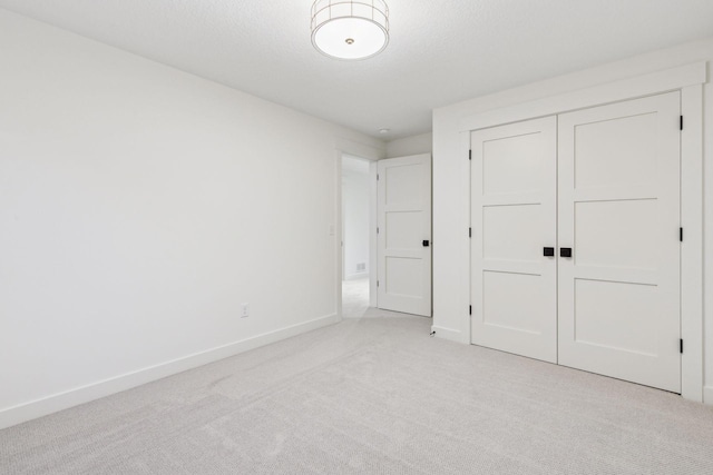 unfurnished bedroom featuring a textured ceiling, baseboards, a closet, and light colored carpet