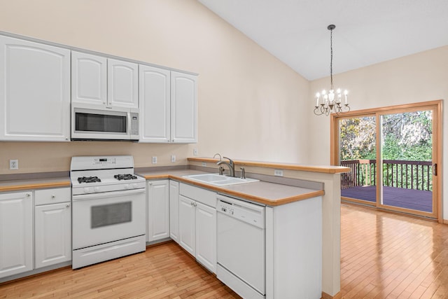 kitchen with vaulted ceiling, a peninsula, an inviting chandelier, white appliances, and a sink