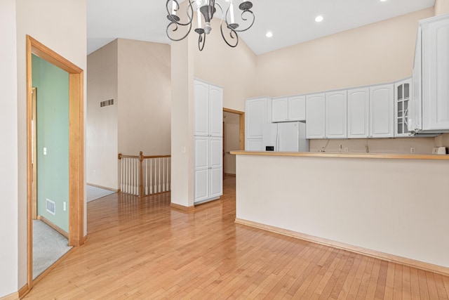 kitchen featuring white cabinets, white refrigerator with ice dispenser, glass insert cabinets, and a towering ceiling