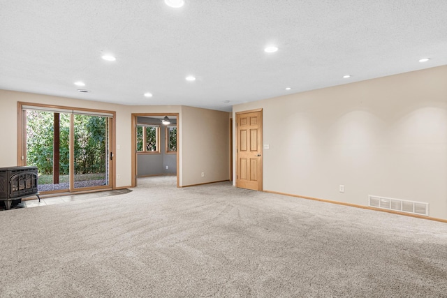 unfurnished living room featuring visible vents, baseboards, light colored carpet, recessed lighting, and a wood stove