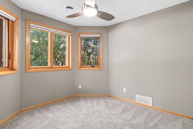 carpeted spare room with a textured ceiling, baseboards, visible vents, and ceiling fan