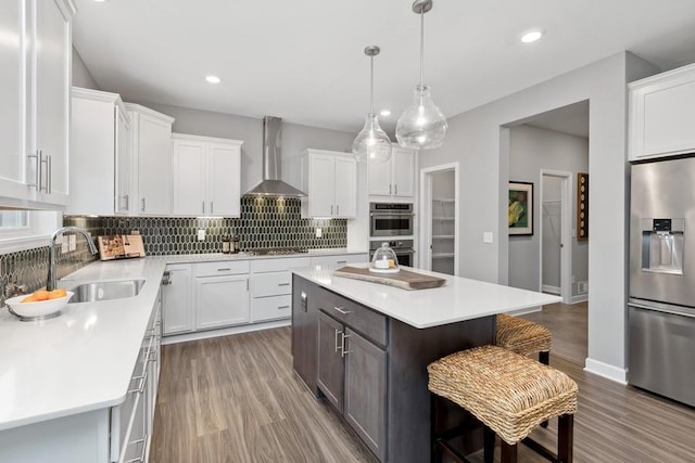 kitchen with sink, wall chimney exhaust hood, appliances with stainless steel finishes, a kitchen island, and white cabinetry