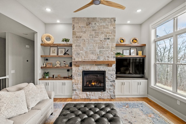 living room with a fireplace, light wood-type flooring, and ceiling fan