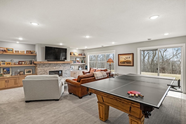 rec room featuring light colored carpet, a stone fireplace, and plenty of natural light