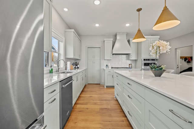 kitchen with sink, premium range hood, backsplash, decorative light fixtures, and appliances with stainless steel finishes