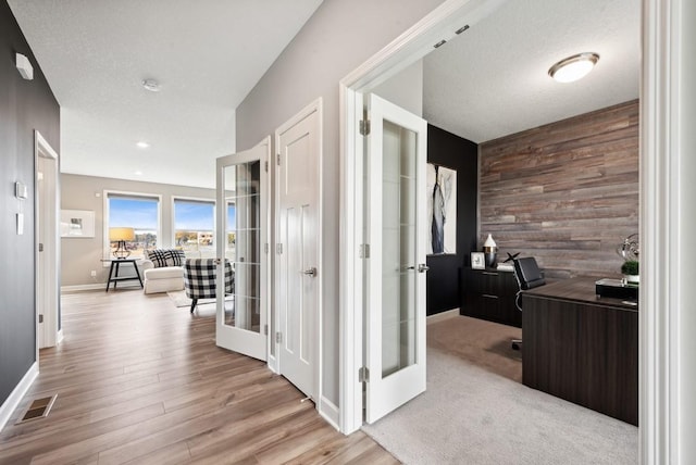 corridor featuring a textured ceiling, light wood-type flooring, french doors, and wooden walls