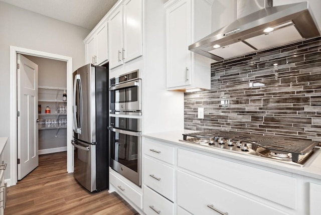 kitchen with appliances with stainless steel finishes, decorative backsplash, wall chimney range hood, white cabinets, and dark wood-type flooring