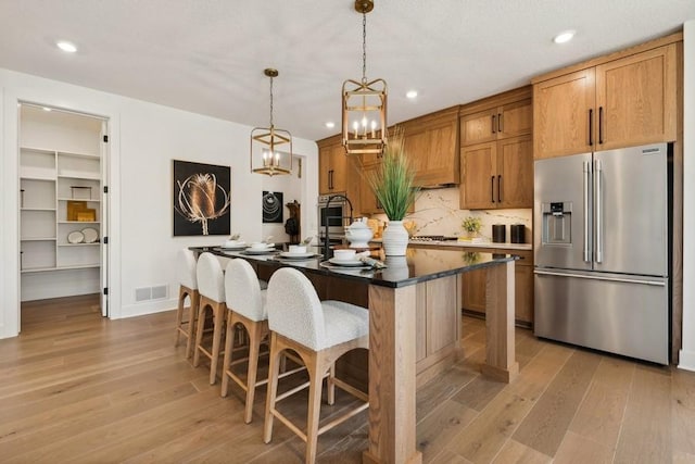 kitchen featuring stainless steel fridge, a kitchen breakfast bar, a chandelier, hanging light fixtures, and an island with sink