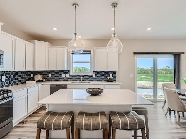 kitchen with appliances with stainless steel finishes, white cabinetry, hanging light fixtures, and a kitchen island