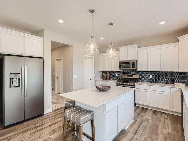 kitchen featuring white cabinets, appliances with stainless steel finishes, a center island, and decorative light fixtures