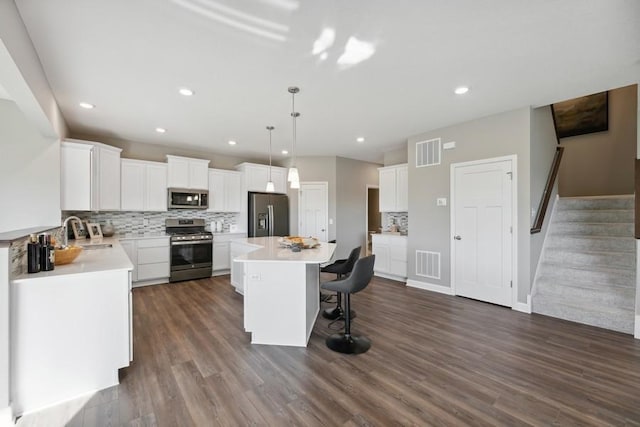 kitchen with appliances with stainless steel finishes, sink, decorative light fixtures, white cabinetry, and a kitchen island