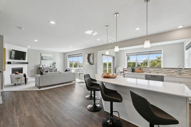 kitchen with sink, decorative light fixtures, dishwasher, dark hardwood / wood-style floors, and a breakfast bar area