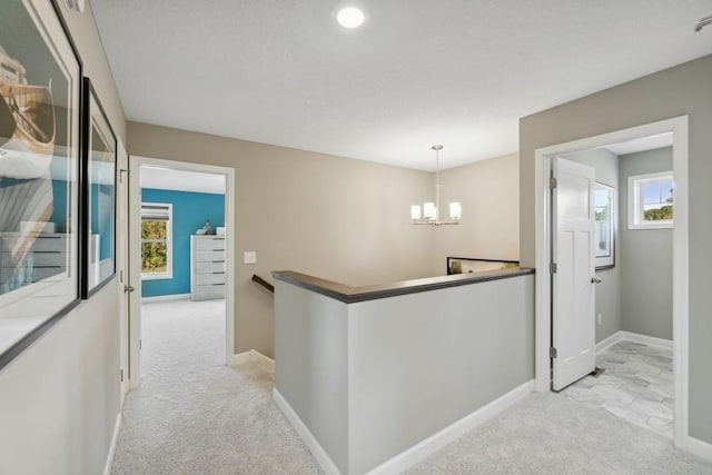 hallway with light carpet, an inviting chandelier, and a healthy amount of sunlight