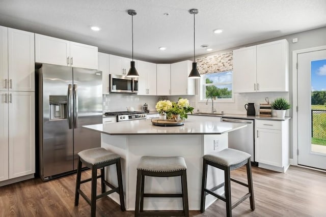 kitchen featuring stainless steel appliances, sink, white cabinets, a center island, and hanging light fixtures