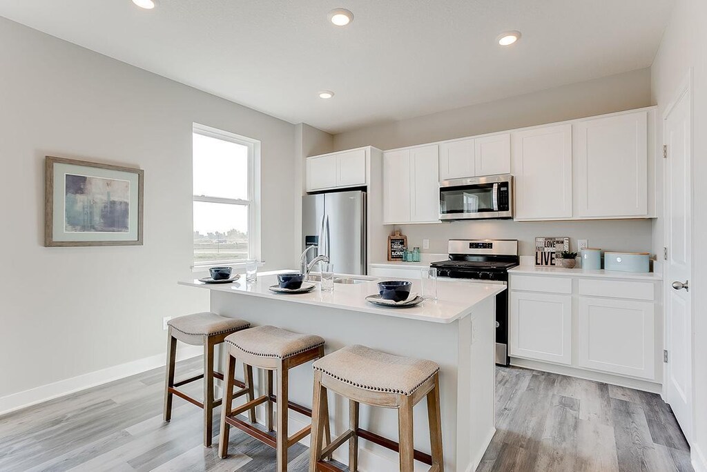kitchen with appliances with stainless steel finishes, light hardwood / wood-style floors, white cabinetry, and an island with sink