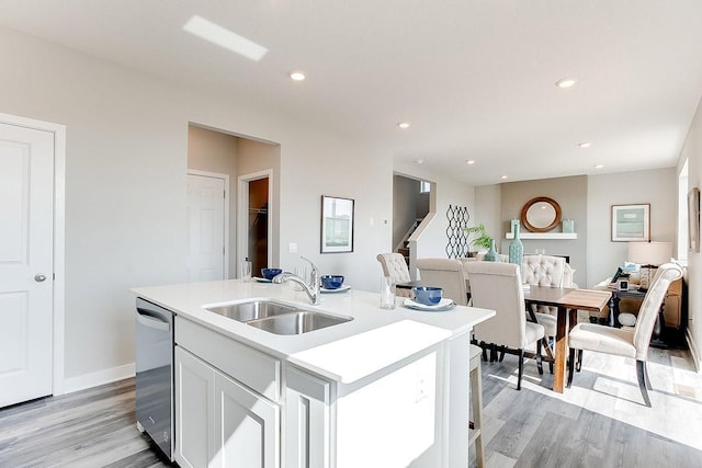 kitchen with dishwasher, a kitchen island with sink, white cabinets, sink, and light hardwood / wood-style flooring