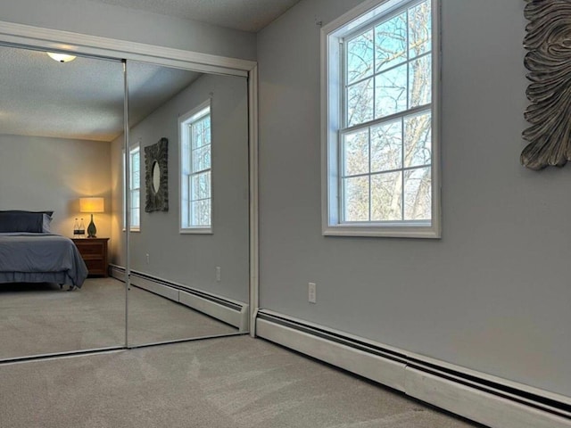 carpeted bedroom featuring a textured ceiling, a closet, and a baseboard heating unit