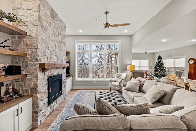 living room featuring light wood-type flooring, a stone fireplace, and ceiling fan