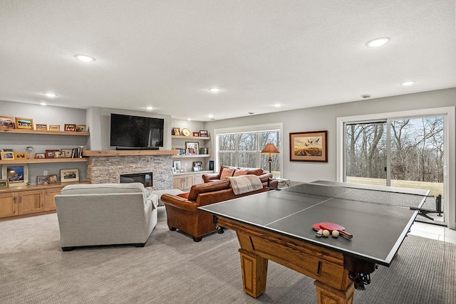 game room featuring light carpet, a textured ceiling, a stone fireplace, and a wealth of natural light