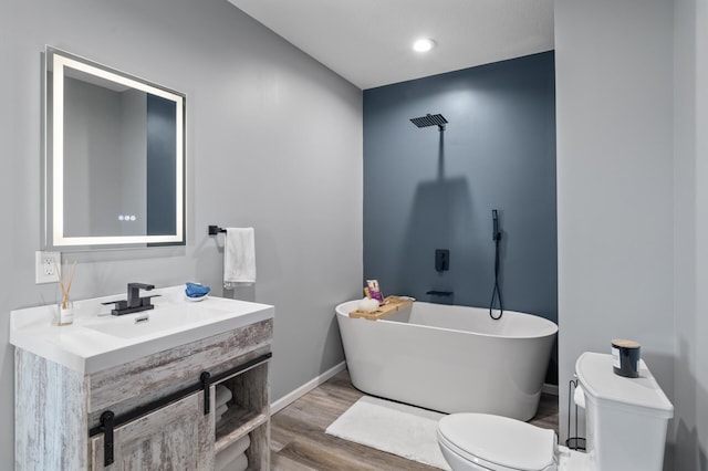 bathroom with baseboards, toilet, a soaking tub, wood finished floors, and vanity