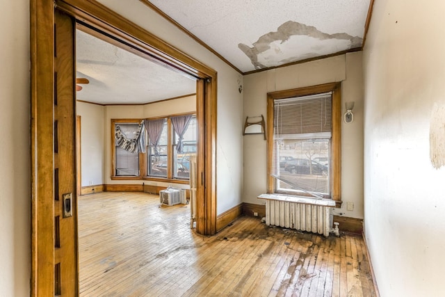 corridor with hardwood / wood-style floors, a textured ceiling, radiator, and ornamental molding