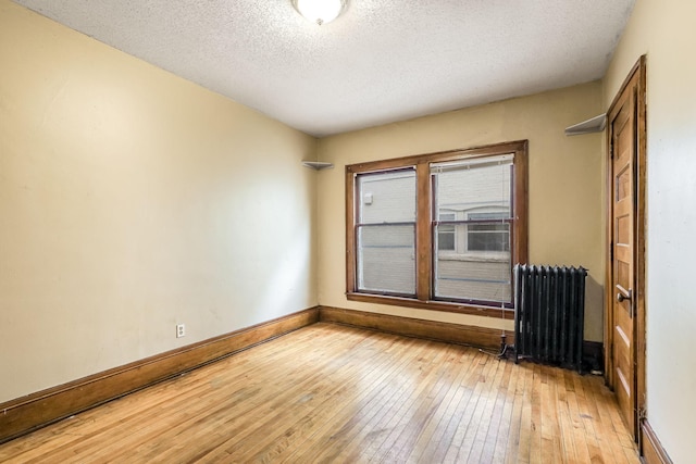 empty room with light hardwood / wood-style floors, a textured ceiling, and radiator