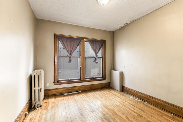 unfurnished room with radiator heating unit, a textured ceiling, and light hardwood / wood-style flooring