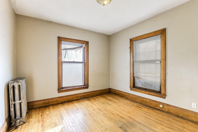 unfurnished room featuring radiator heating unit, a textured ceiling, and light hardwood / wood-style flooring