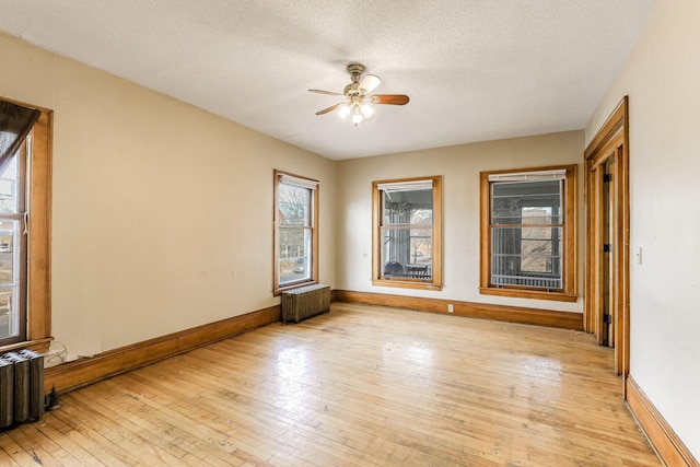 empty room with ceiling fan, a textured ceiling, radiator, and light hardwood / wood-style flooring