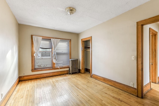 unfurnished bedroom with light wood-type flooring, a textured ceiling, radiator, and a closet