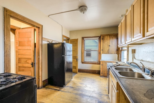 kitchen with black refrigerator, sink, light hardwood / wood-style flooring, white gas range, and plenty of natural light