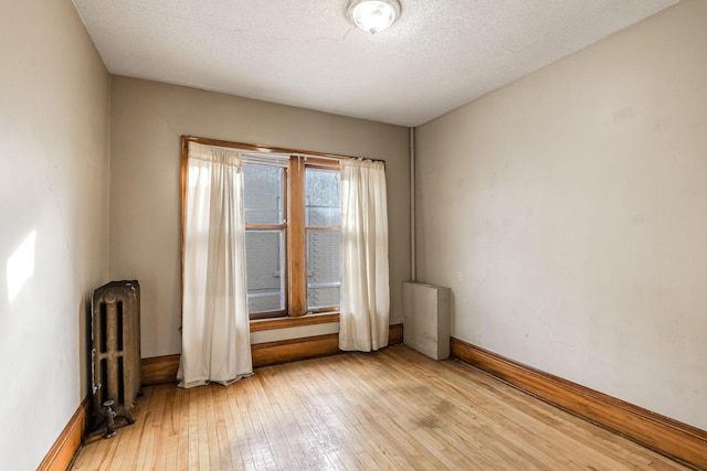 empty room with radiator heating unit, a textured ceiling, and light hardwood / wood-style flooring