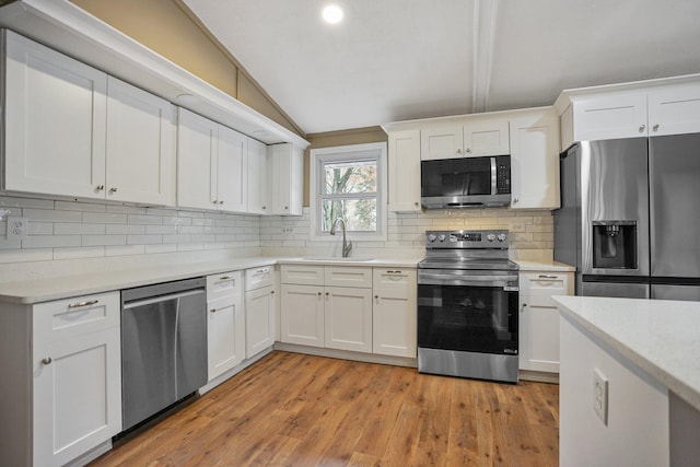 kitchen featuring sink, white cabinetry, stainless steel appliances, and vaulted ceiling