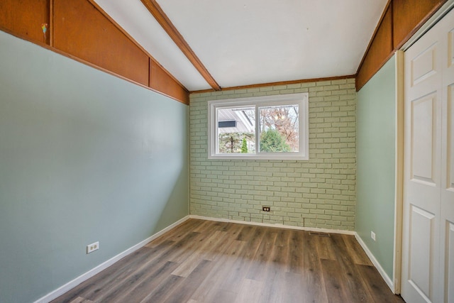 unfurnished bedroom featuring dark hardwood / wood-style flooring, brick wall, and lofted ceiling