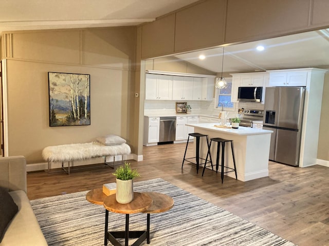 kitchen with a center island, stainless steel appliances, decorative light fixtures, a breakfast bar, and white cabinets