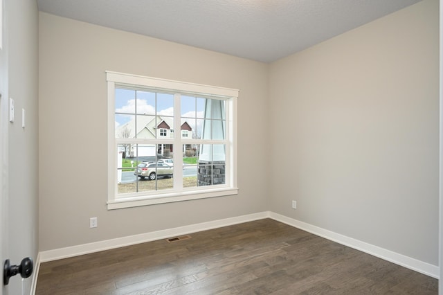 empty room with dark wood-style floors, visible vents, and baseboards