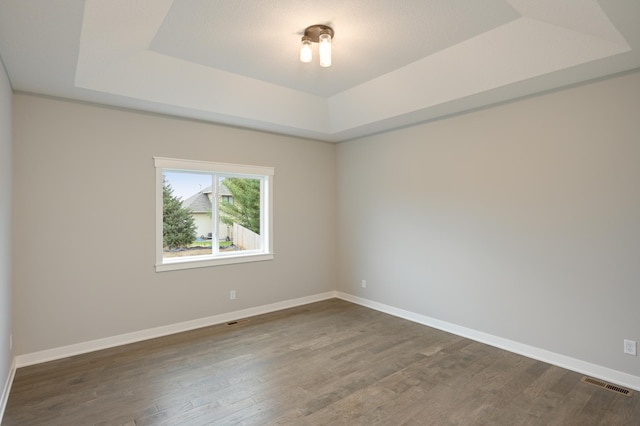 spare room with dark wood-style flooring, a tray ceiling, baseboards, and visible vents