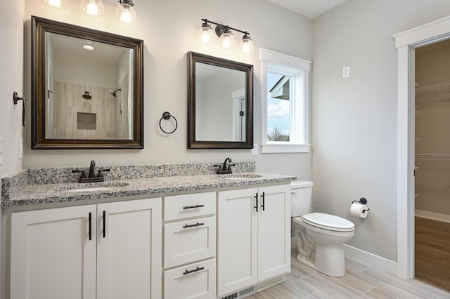 full bathroom with toilet, a sink, double vanity, and baseboards